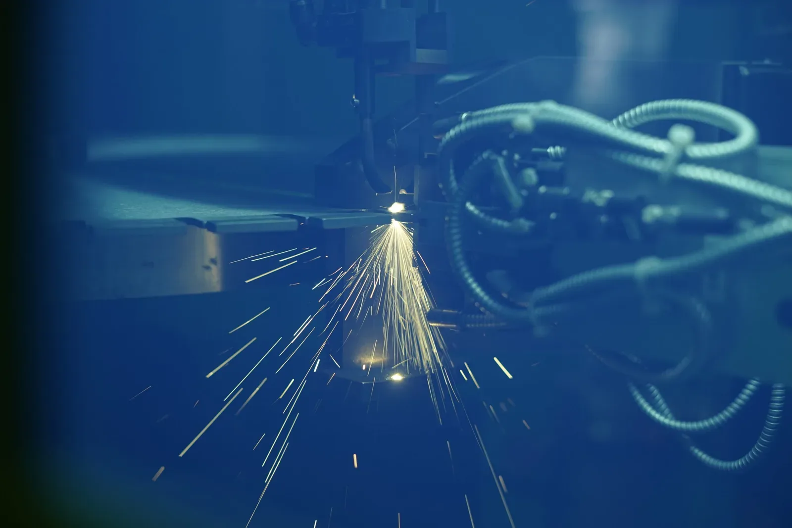 Sparks spraying from a laser welding head as it runs a weld along the rim of a blade.