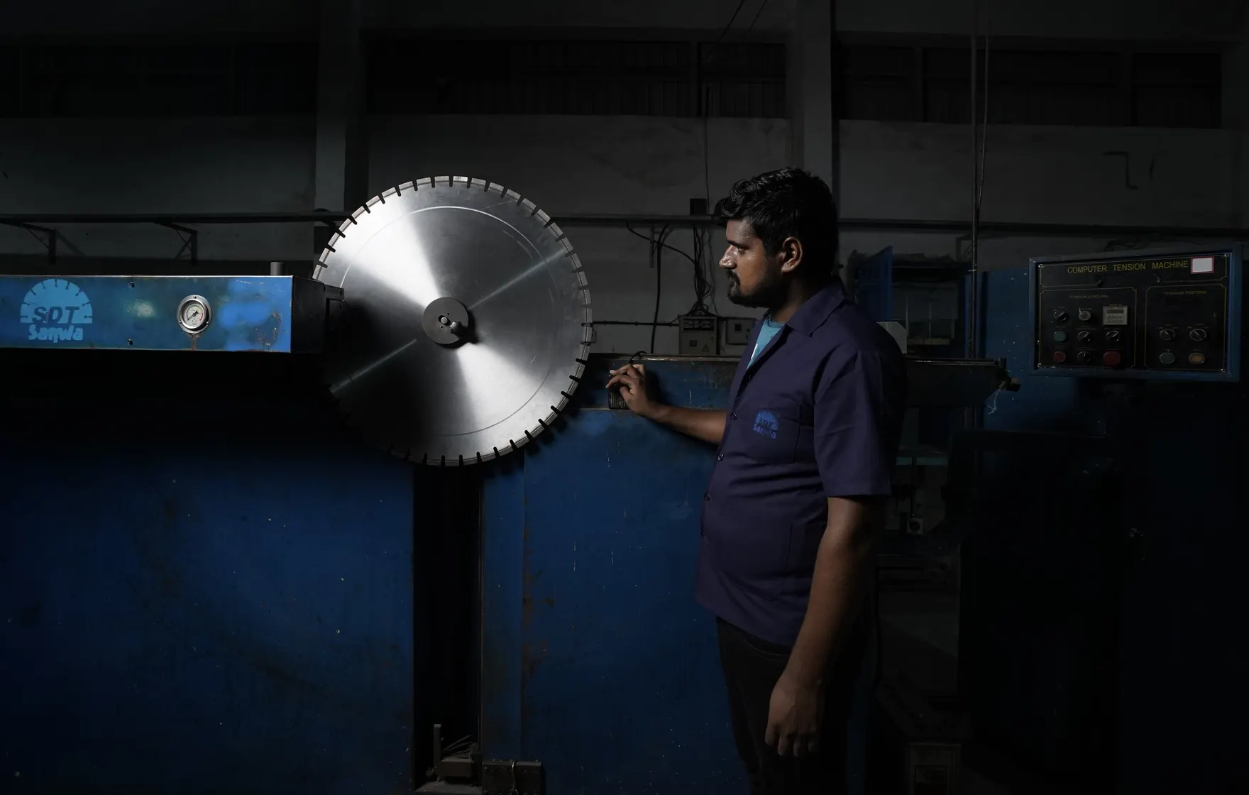 A large saw blade held in a computer tension machine on the factory floor, with a technician beside it.